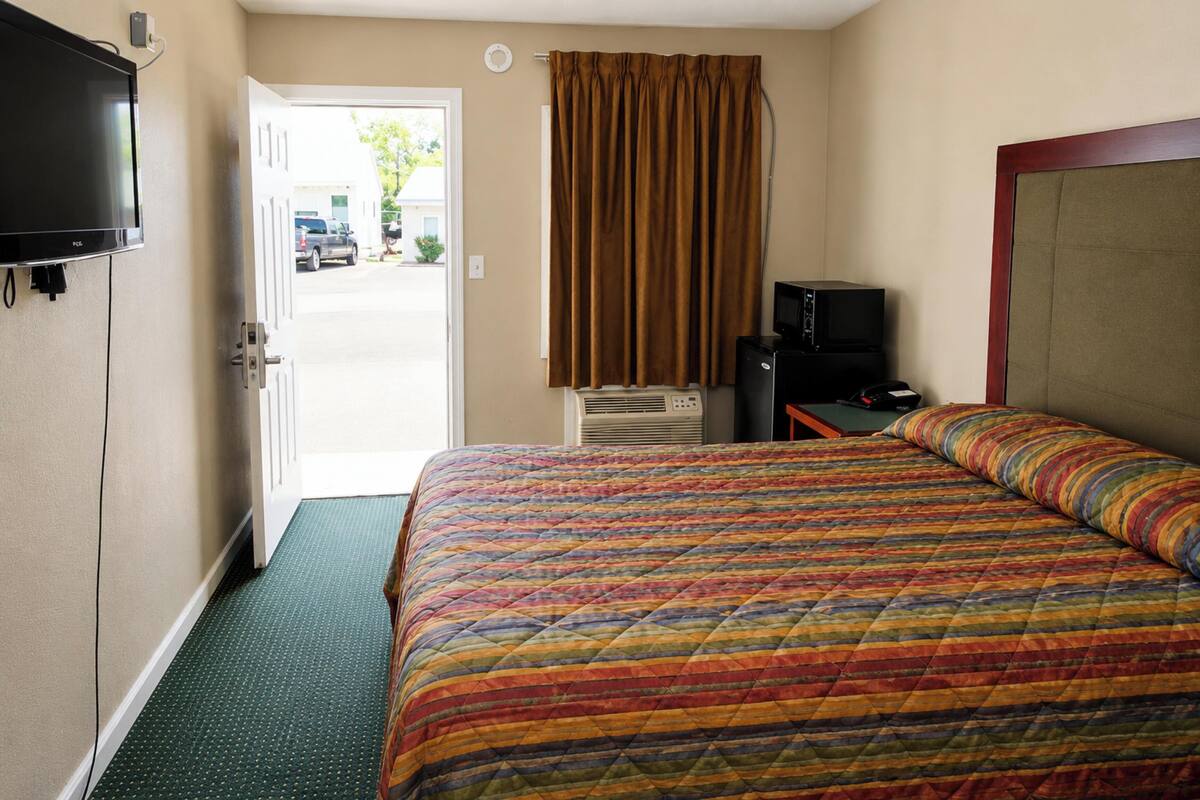 A hotel room with a bed, a television, an air conditioning unit, and a view of the outside.