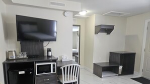 A compact hotel room with a kitchenette, a flat-screen TV, a white chair, and a bed in the background. - Leelas Villa Inn Flesherton (Grey Highlands)