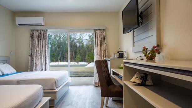 A hotel room with two beds, a desk, a chair, a TV, and a view of the outdoors. - Leelas Villa Inn Flesherton (Grey Highlands)