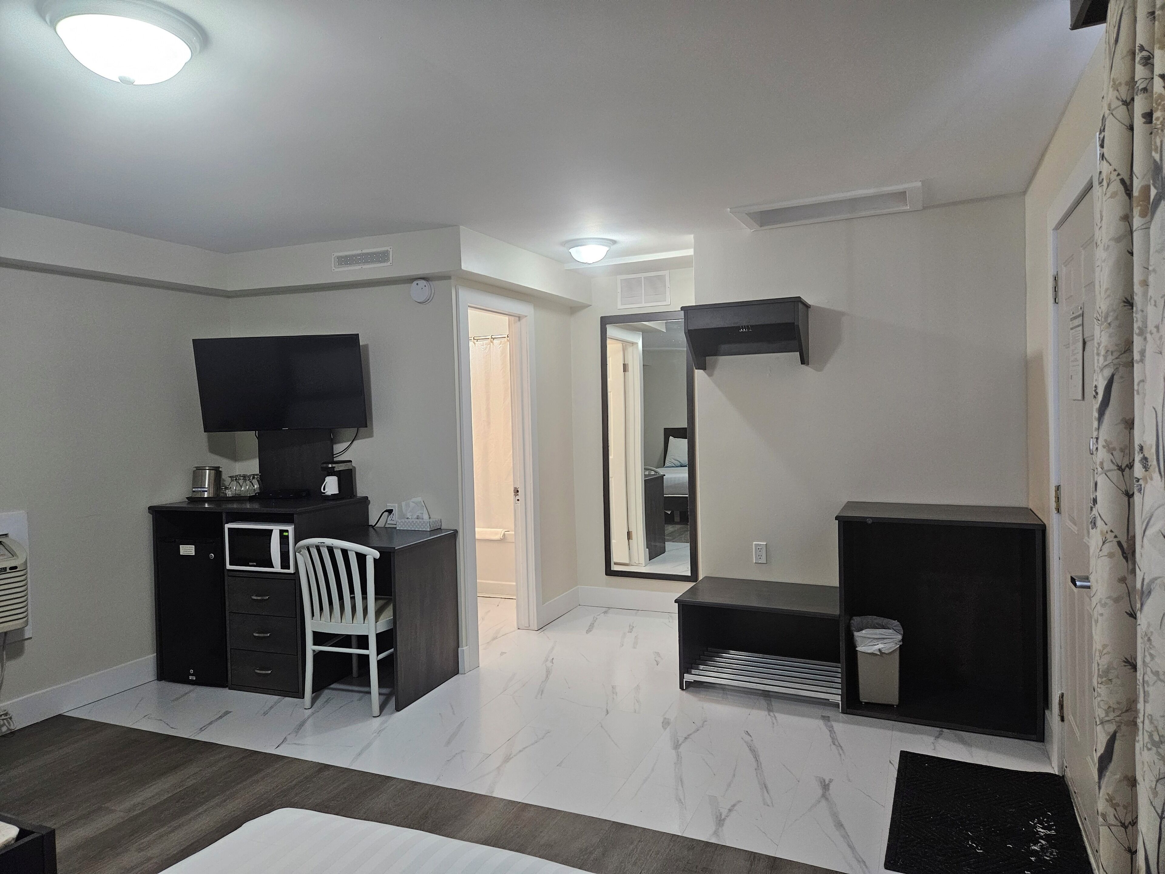 A hotel room with a desk, chair, television, and a large mirror.