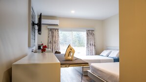 A hotel room with a flat-screen TV mounted on the wall, a desk with a computer and a vase of flowers, two beds with white bedding, and a window with curtains. - Leelas Villa Inn Flesherton (Grey Highlands)