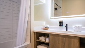 A modern bathroom with a bathtub, a large mirror, a sink with a faucet, and shelves with towels. - Leelas Villa Inn Flesherton (Grey Highlands)