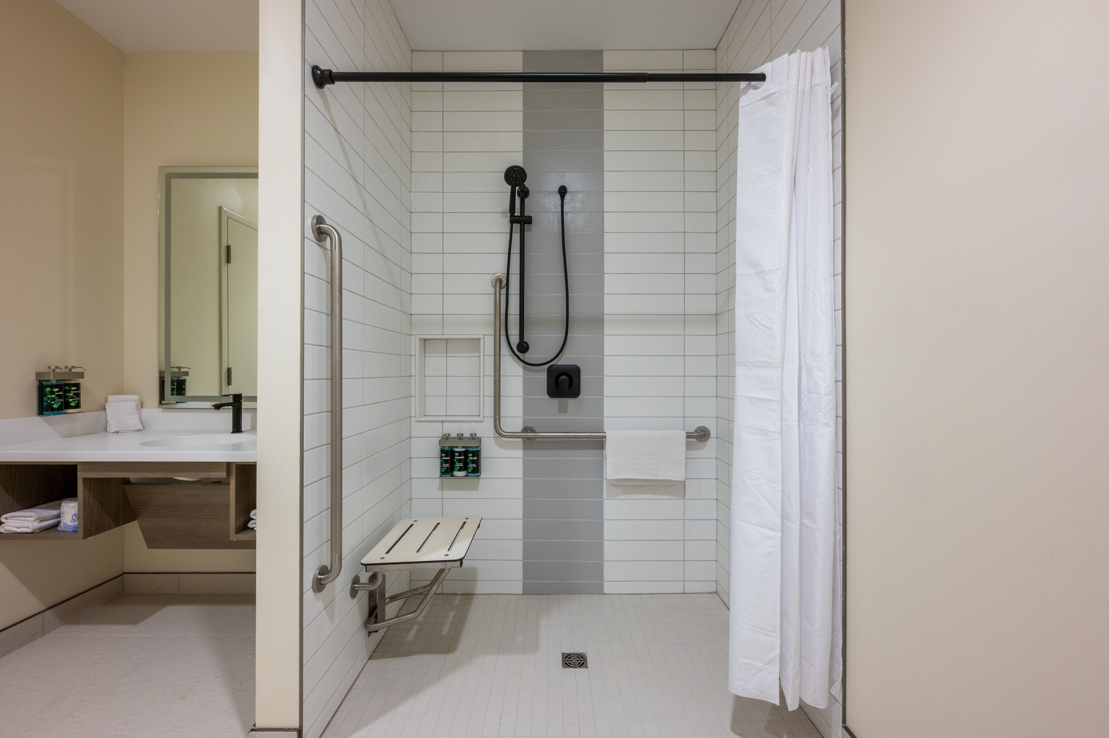 A modern bathroom with a shower, grab bar, and a bench.