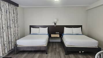Ein Hotelzimmer mit zwei Betten, einem Nachttisch, einer Lampe und einem Fenster mit Vorhängen.