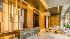 A modern interior with a marble reception desk, a seating area with sofas, and a stone wall. - Global Luxury Suites at Newport (Jersey City)