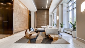 A modern lobby with a sofa, coffee table, and potted plants. - Global Luxury Suites at Newport (Jersey City)