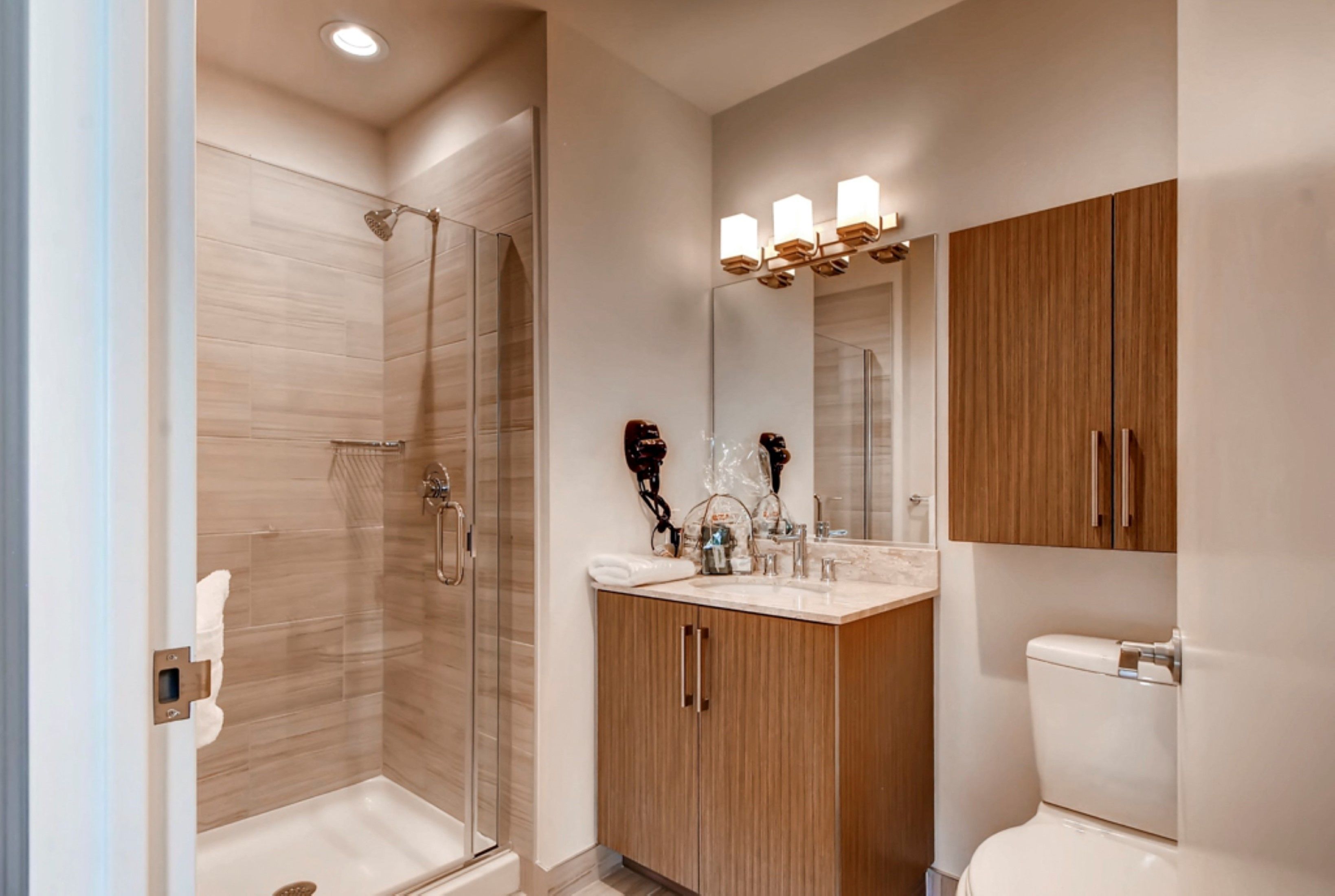 Een moderne badkamer met een douche met glazen wand, een houten wastafelmeubel met spiegel, en een toilet.
