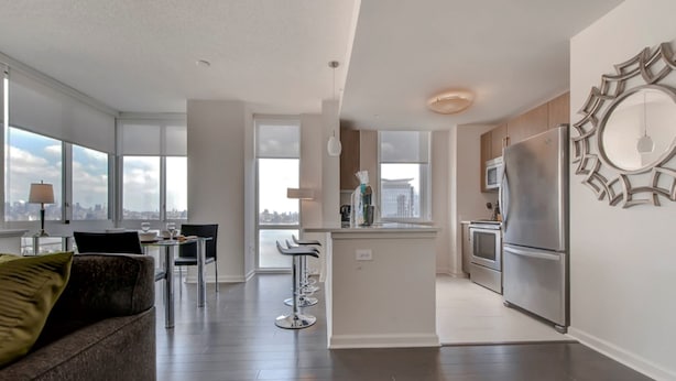 A modern apartment with a living room, dining area, kitchen, and large windows offering city views. - Global Luxury Suites at Newport (Jersey City)