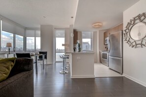 Eine moderne Wohnung mit Wohnzimmer, Essbereich, Küche und großen Fenstern mit Blick auf die Stadt.