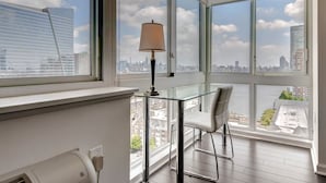 A modern room with a glass table, a chair, and a lamp. It features large windows with a city view. - Global Luxury Suites at Newport (Jersey City)