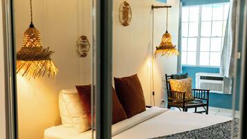 Un dormitorio con cama, almohadas, una silla y lámparas colgantes.