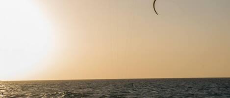 Una persona practicando kitesurf en el océano, con un atardecer de fondo.