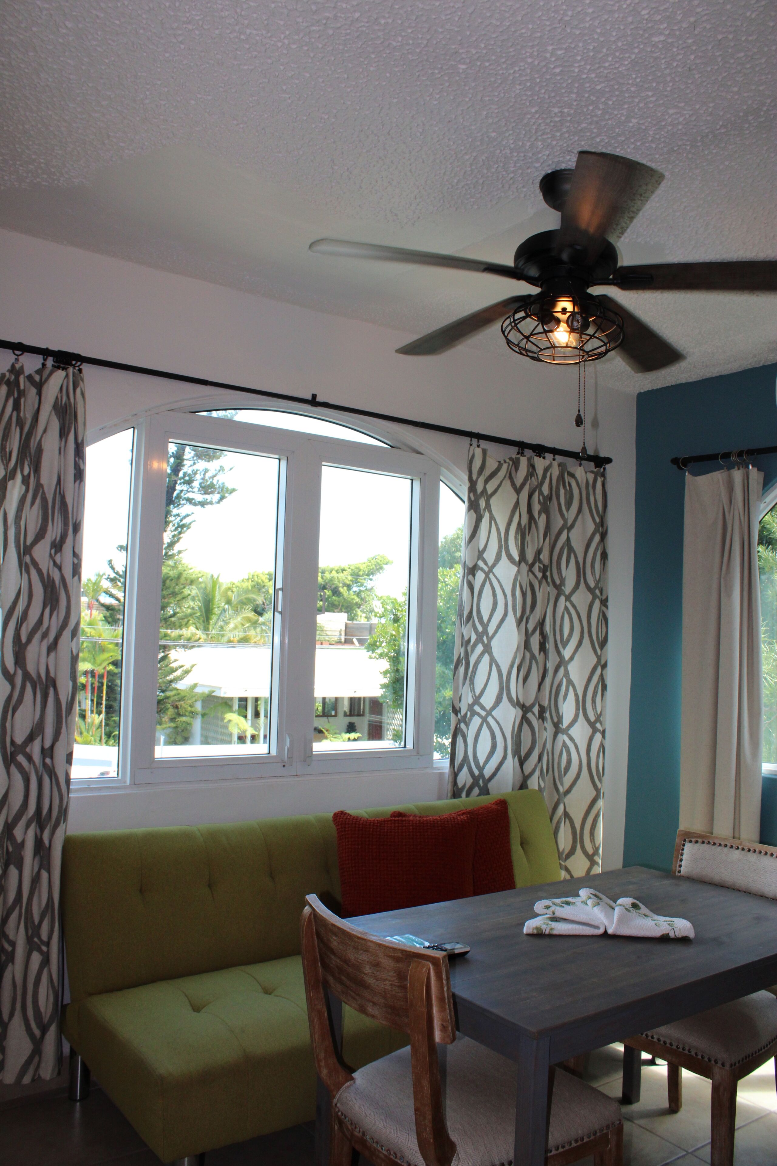 A room with a dining table, chairs, a green sofa, and a ceiling fan.
