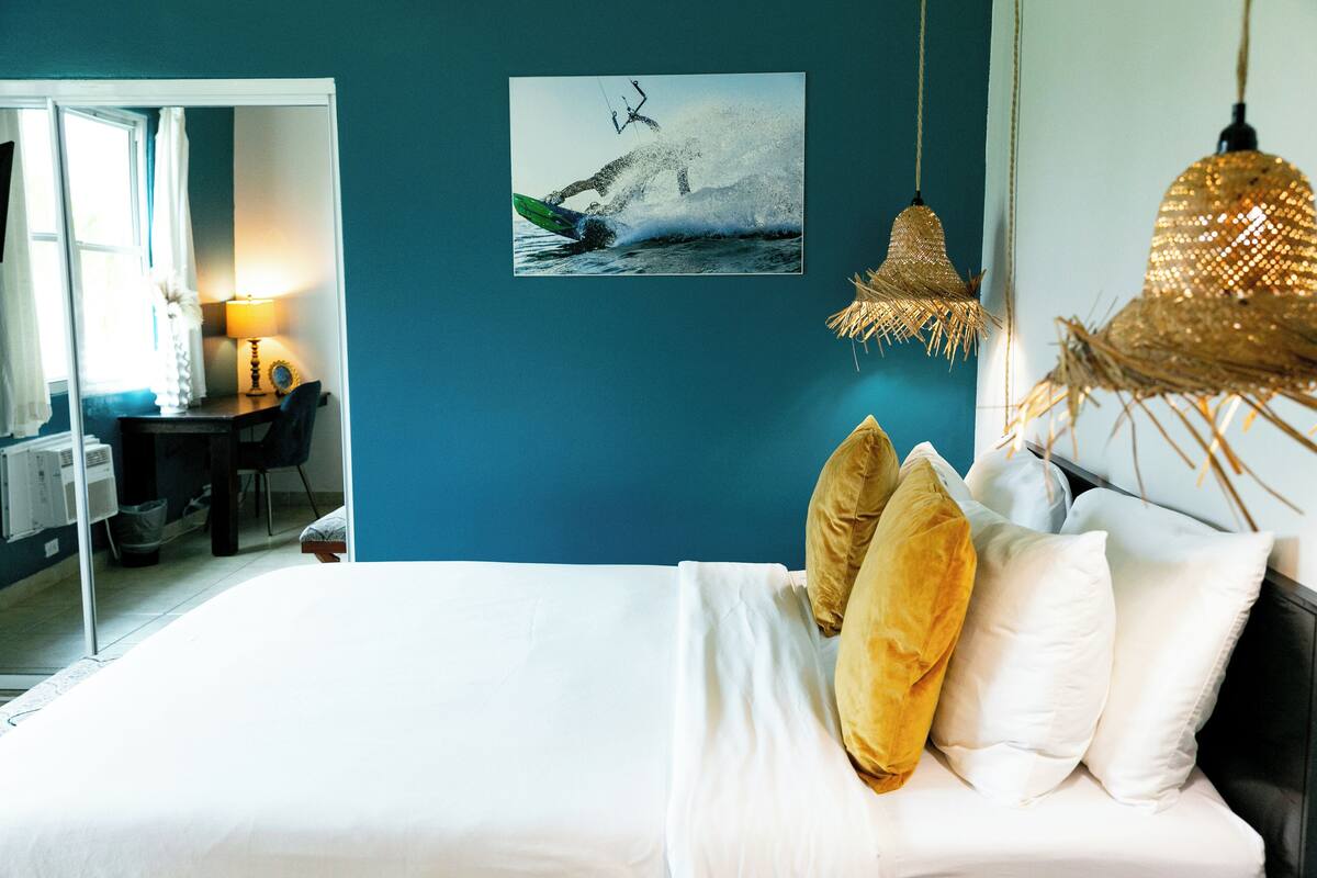 A bedroom with a bed, pillows, a desk, a chair, and a wall-mounted picture.