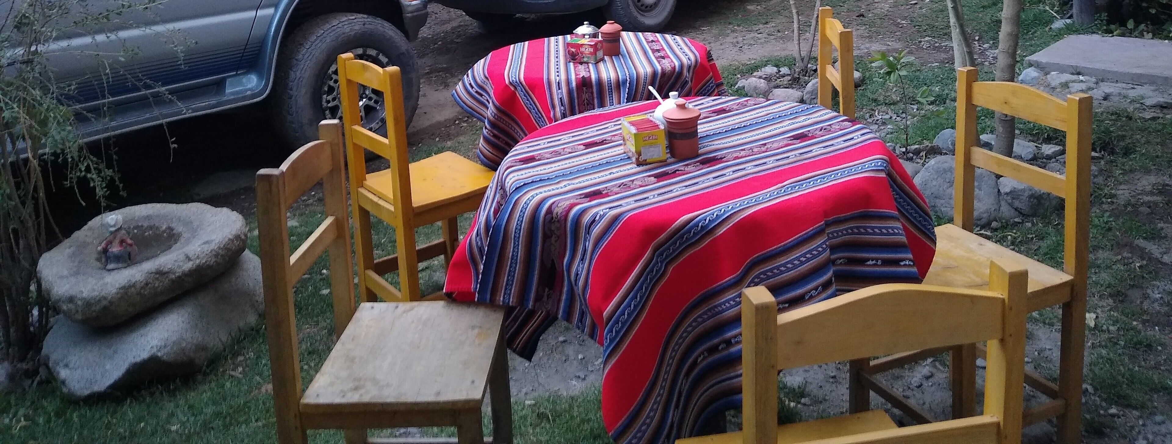 An outdoor dining area with a table covered by a colorful striped tablecloth, surrounded by wooden chairs.
