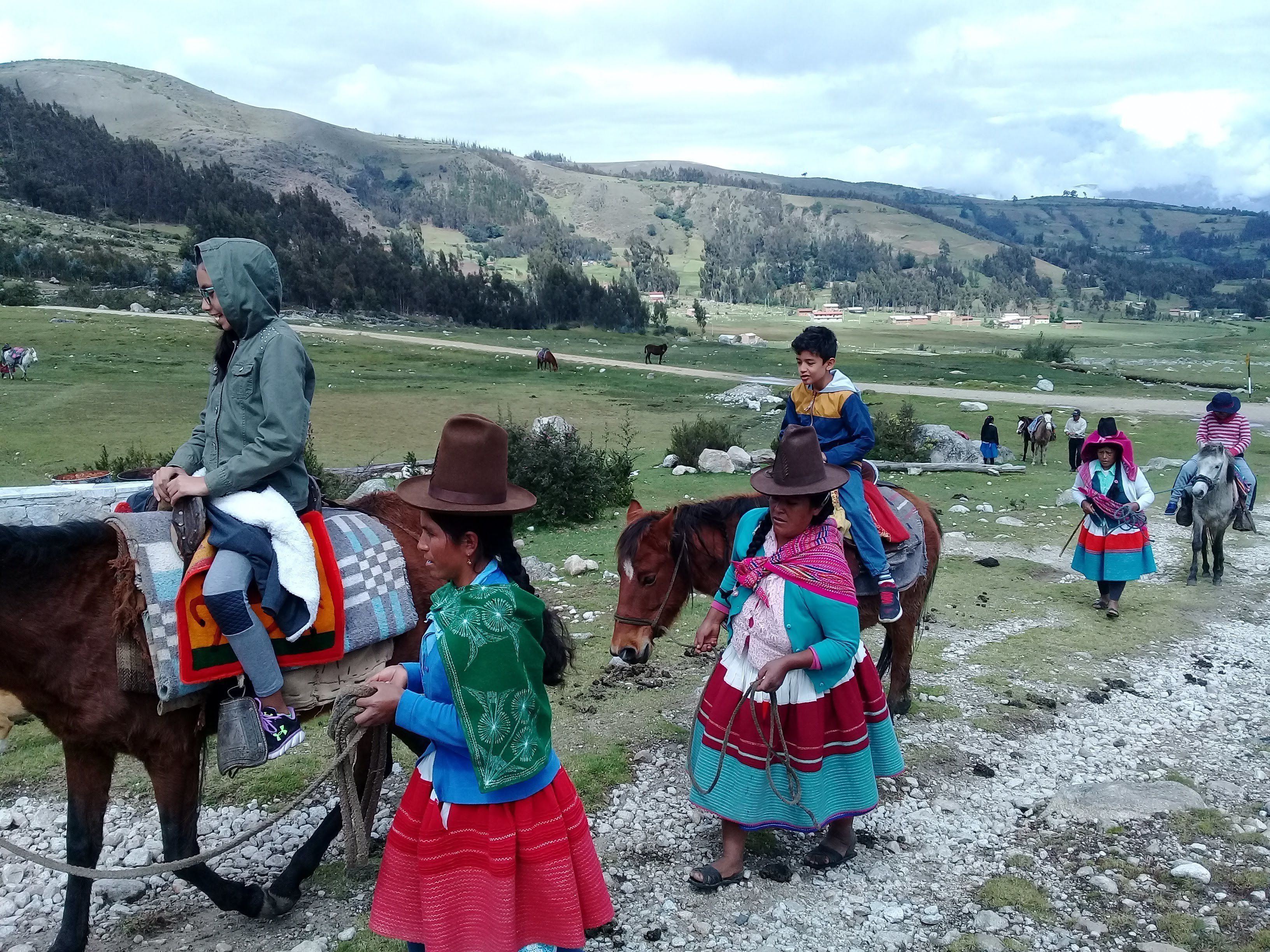 A rural landscape with people riding horses and walking.