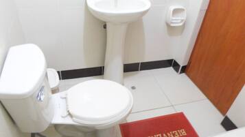 Ein Badezimmer mit Toilette, Waschbecken und einer roten Matte mit dem Schriftzug 'BIENVENIDO'.