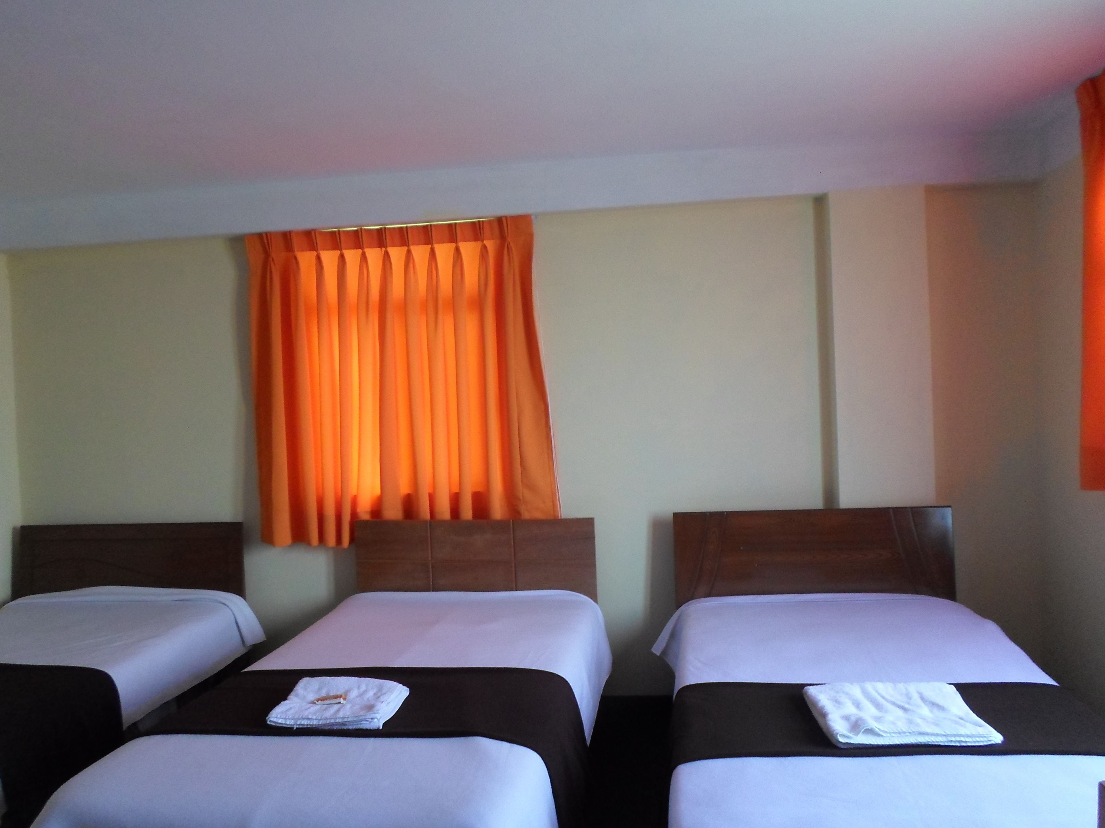 Ett hotellrum med två separata sängar, en sänggavel i trä och ett fönster med orangefärgade gardiner.