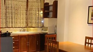 Cocina compacta con armarios de madera, una mesa de comedor con sillas y un ventanal con cortinas.