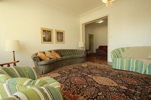 A living room with a grey sofa, striped armchairs, a patterned rug, and two framed floral paintings on the wall.