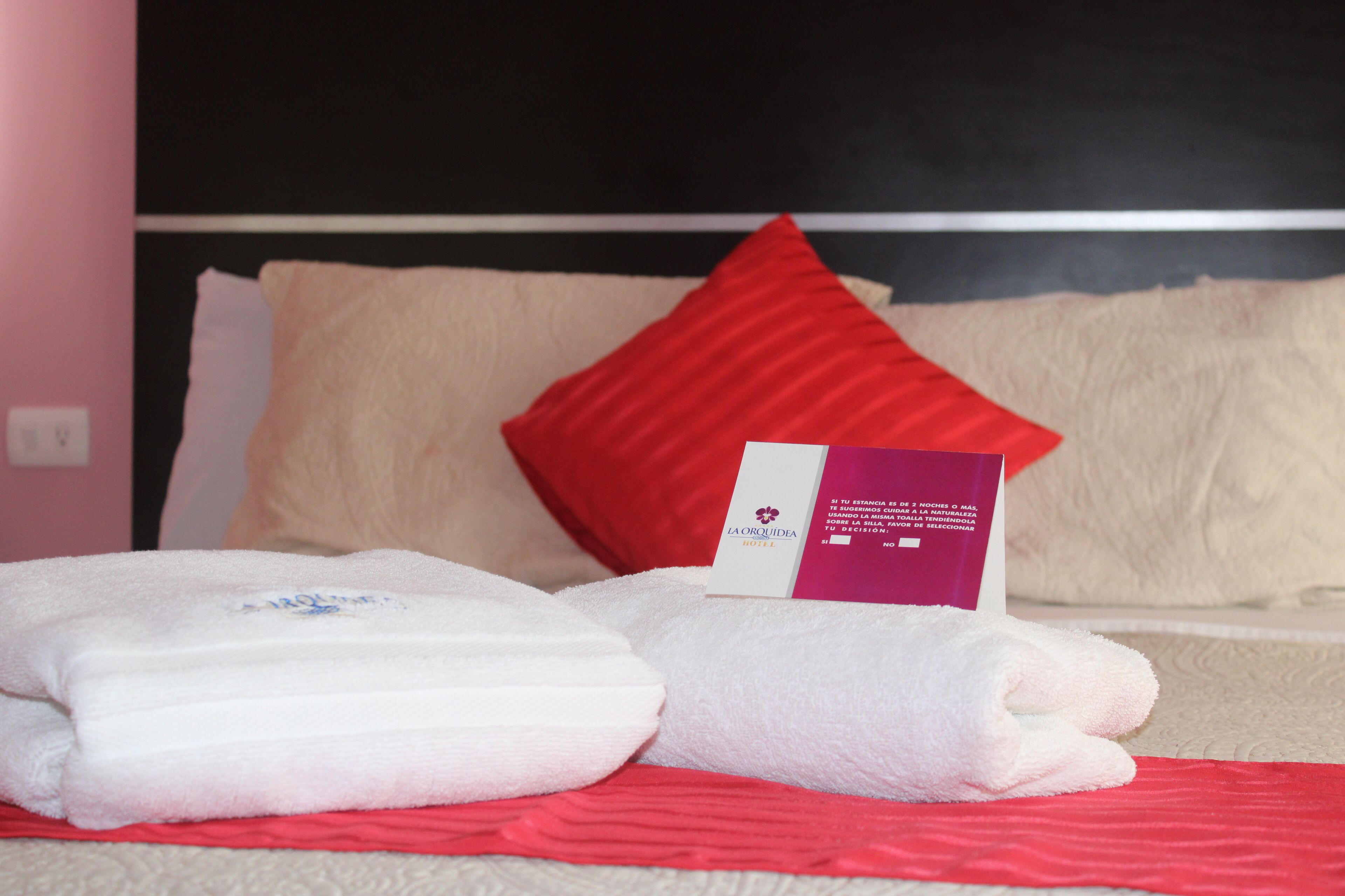 Un letto rifatto con asciugamani bianchi e rossi, un cuscino rosso e un biglietto sul letto.