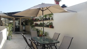 Een terras met een glazen tafel en stoelen, een parasol en potplanten.