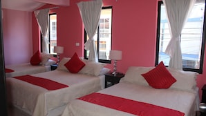 Een hotelkamer met roze wanden, twee bedden met rode en witte beddengoed, en een raam met gordijnen.