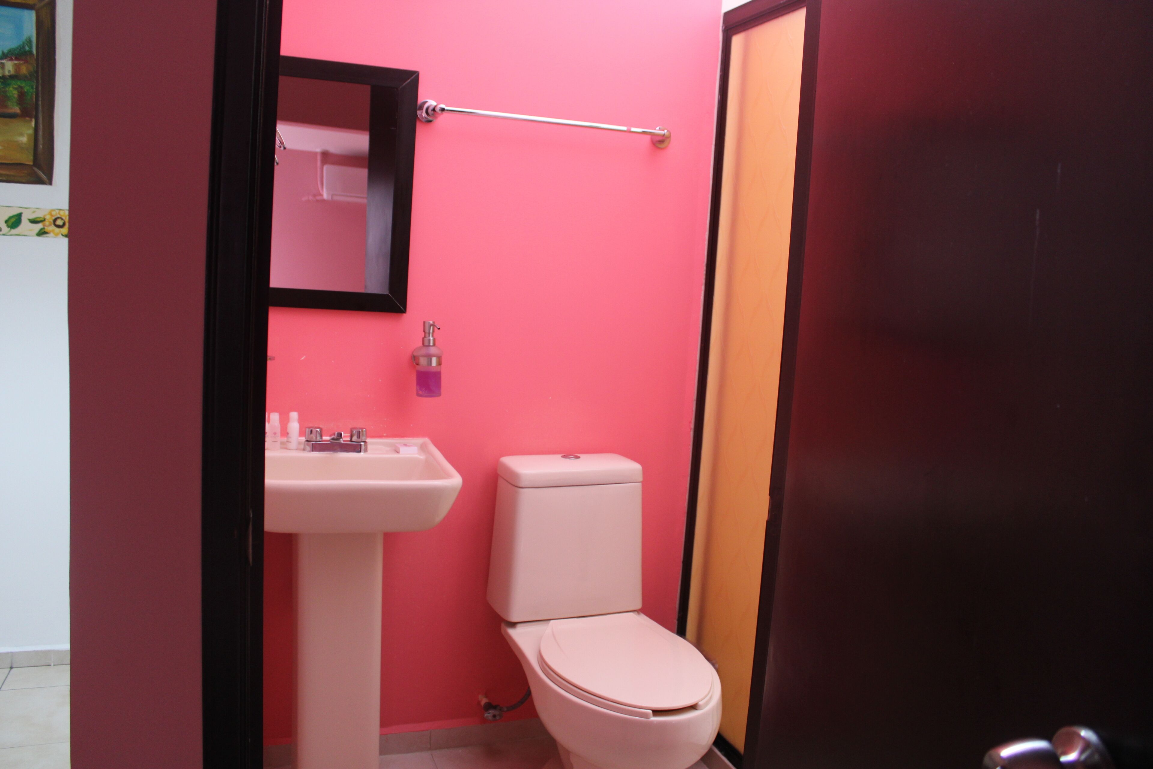 Un baño con pared rosa, lavamanos blanco y retrete.