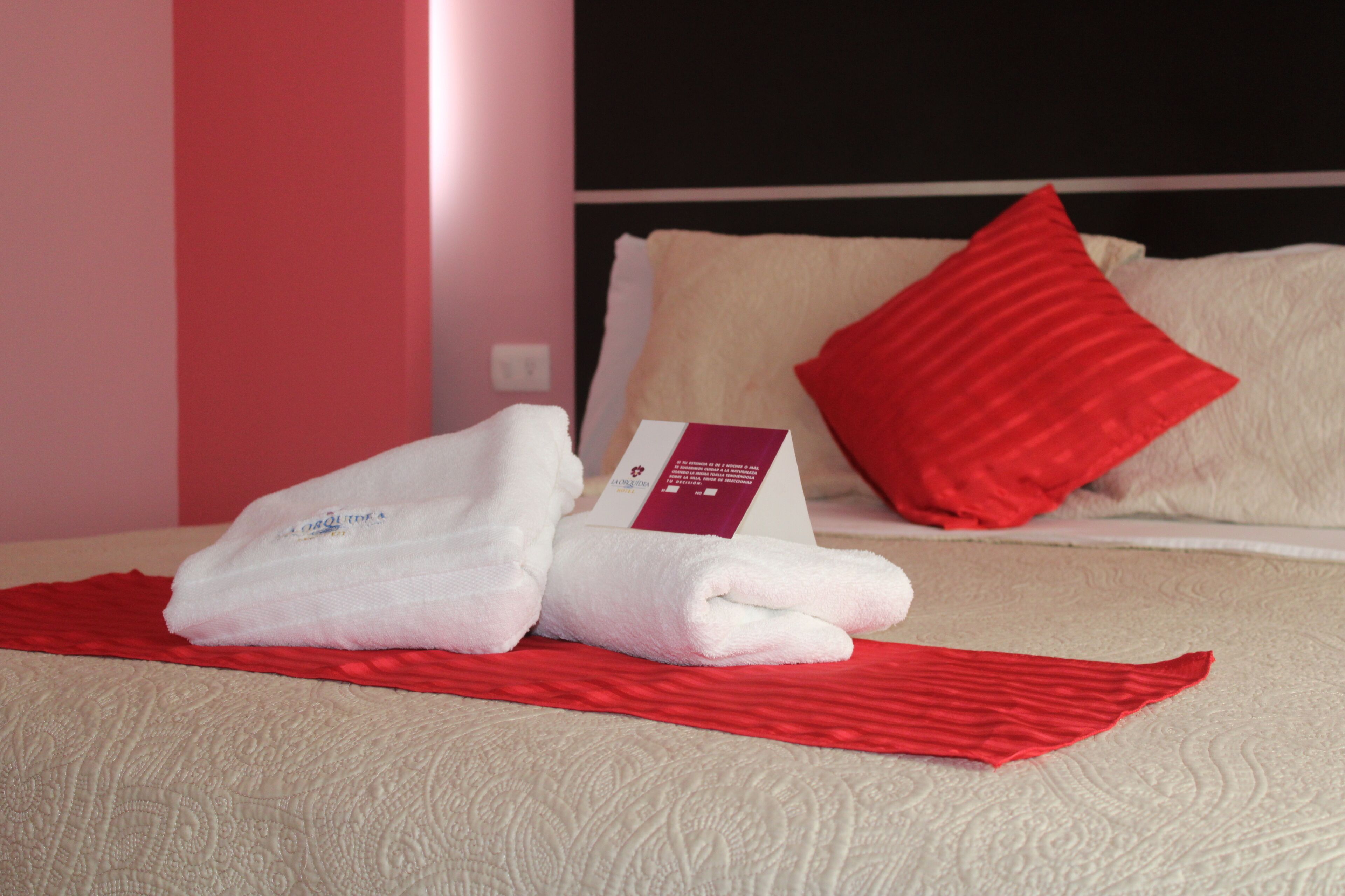 Un lit bien fait, avec un oreiller rouge, une serviette blanche pliée et une couverture rouge.