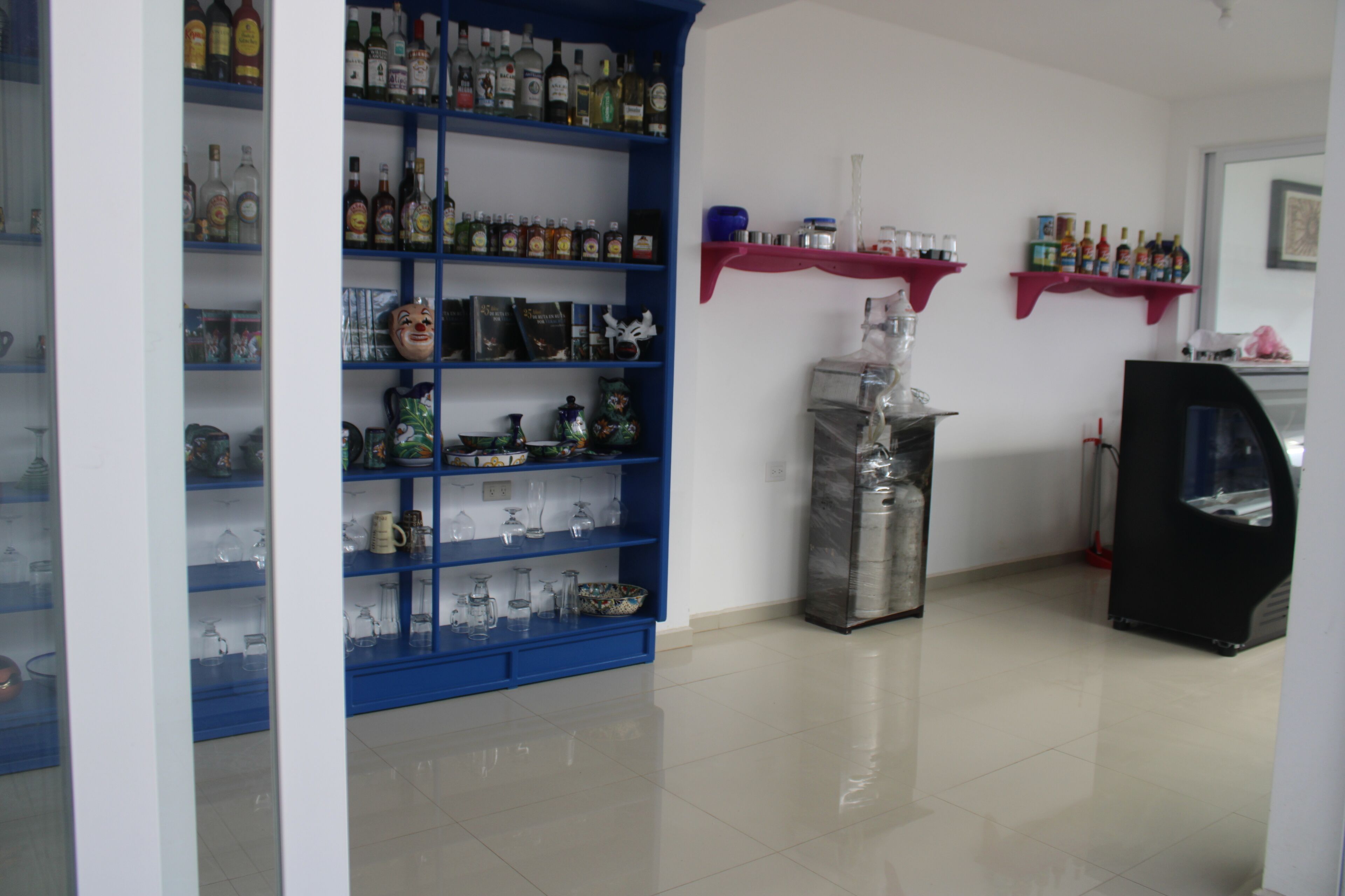 A room with blue shelving units filled with various bottles and glassware, a metal container, and a black cabinet.
