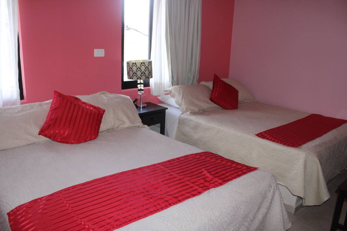 Ein Hotelzimmer mit zwei Betten, jeweils mit einer rot-weißen Bettdecke, und einem Nachttisch mit einer Lampe dazwischen.