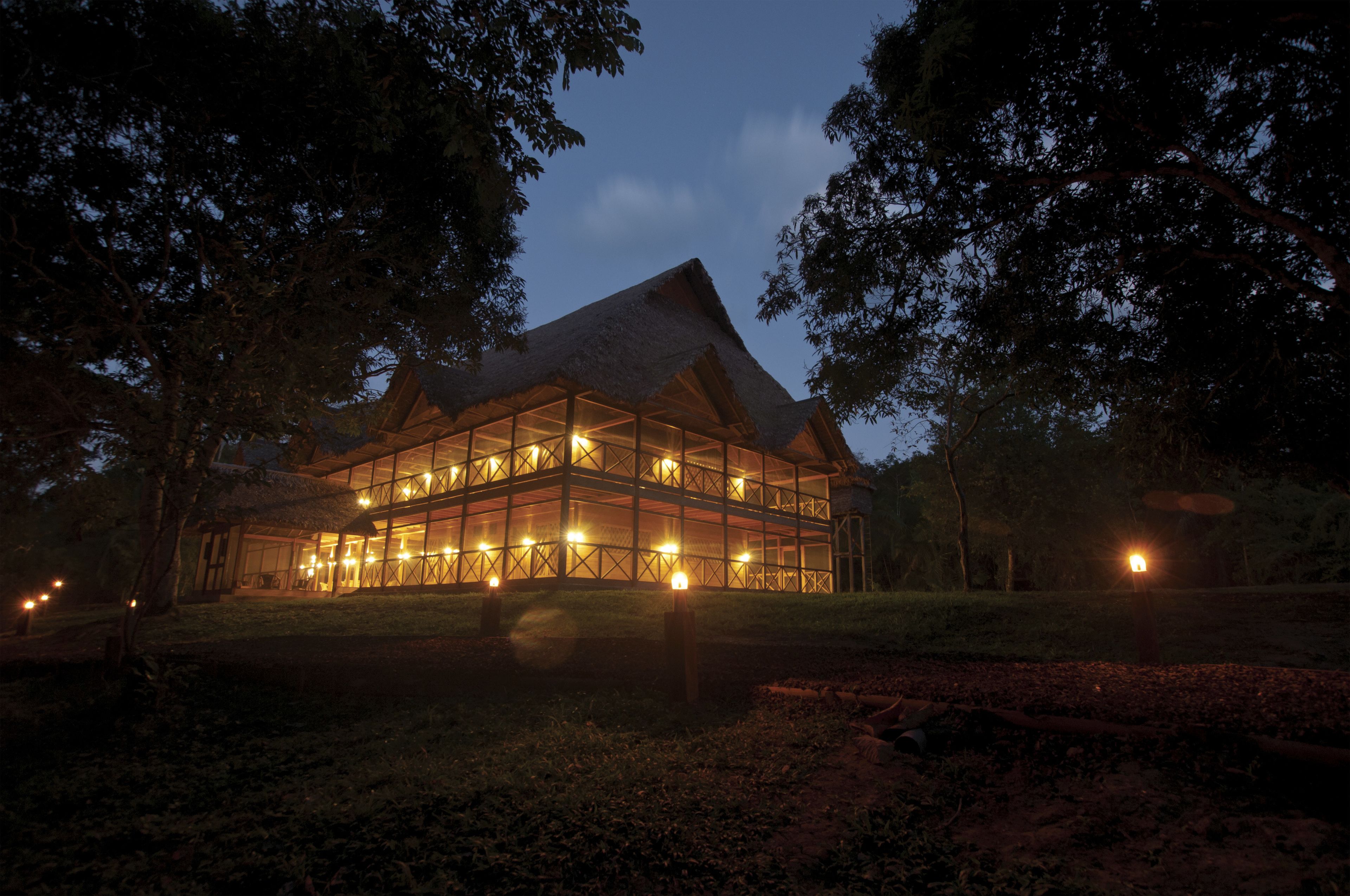 A large, illuminated building with a thatched roof, surrounded by trees.