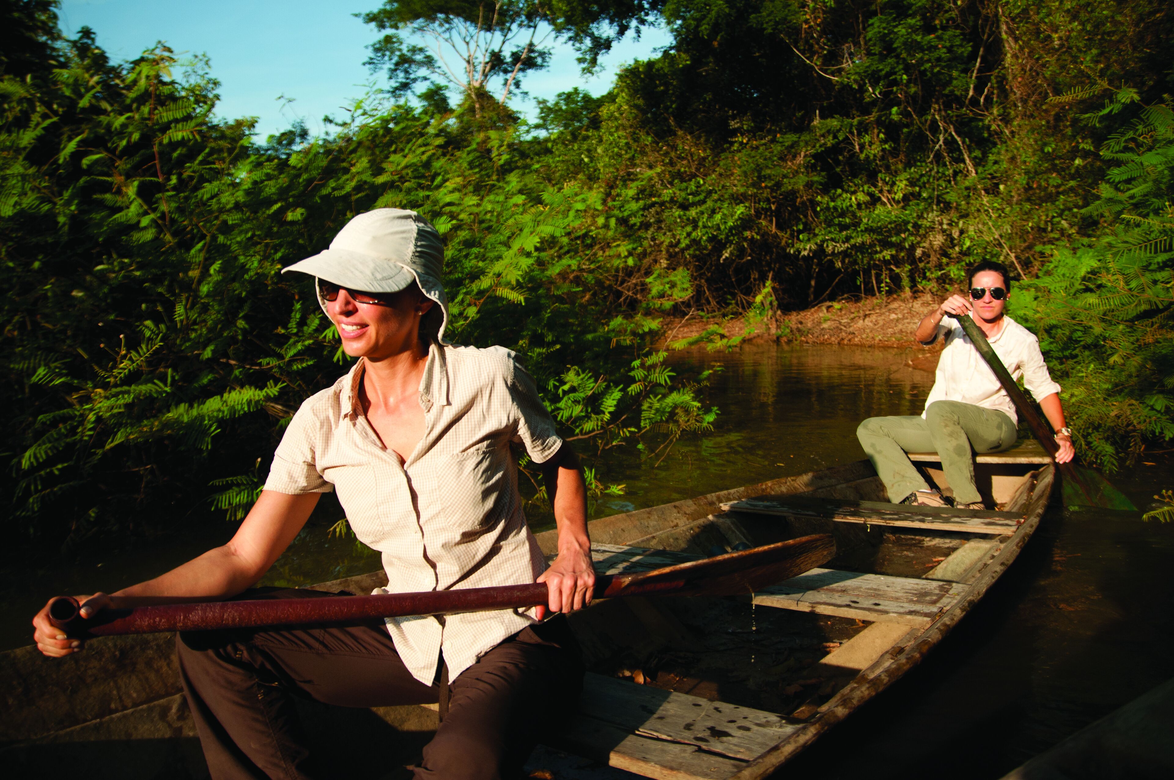 Two people in a canoe on a river surrounded by dense greenery.