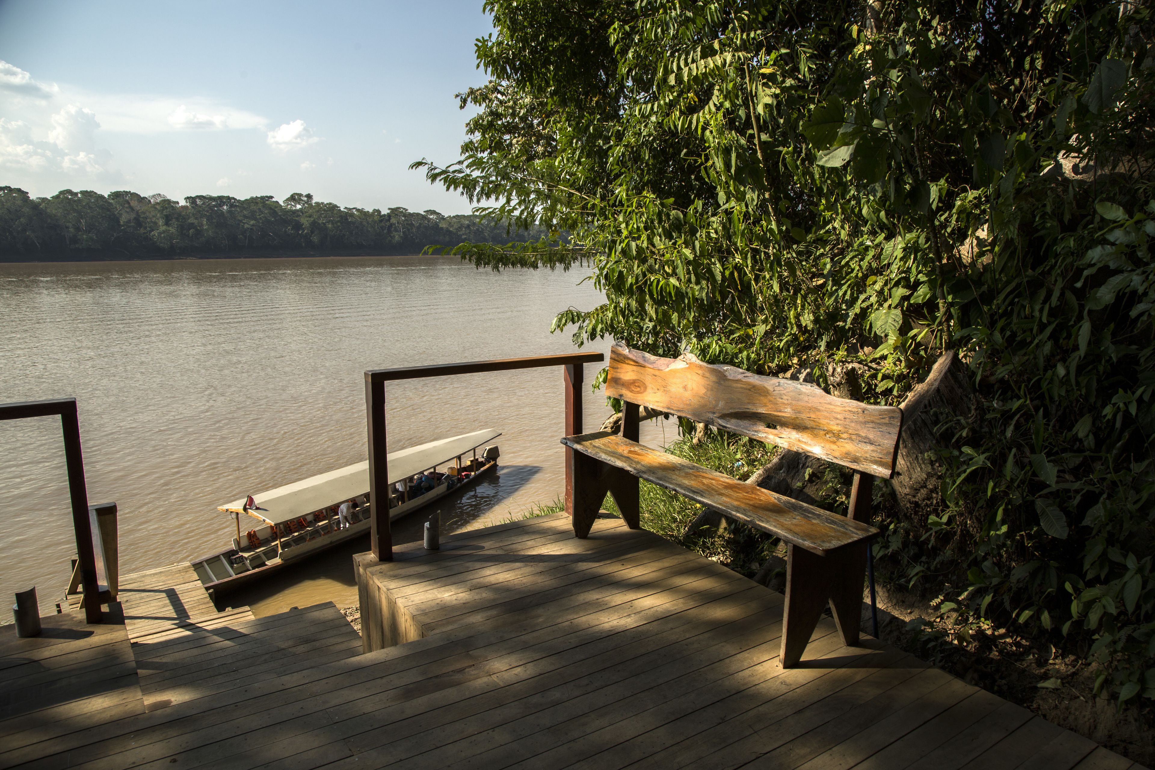 A wooden deck with a bench overlooking a calm lake, surrounded by lush greenery.