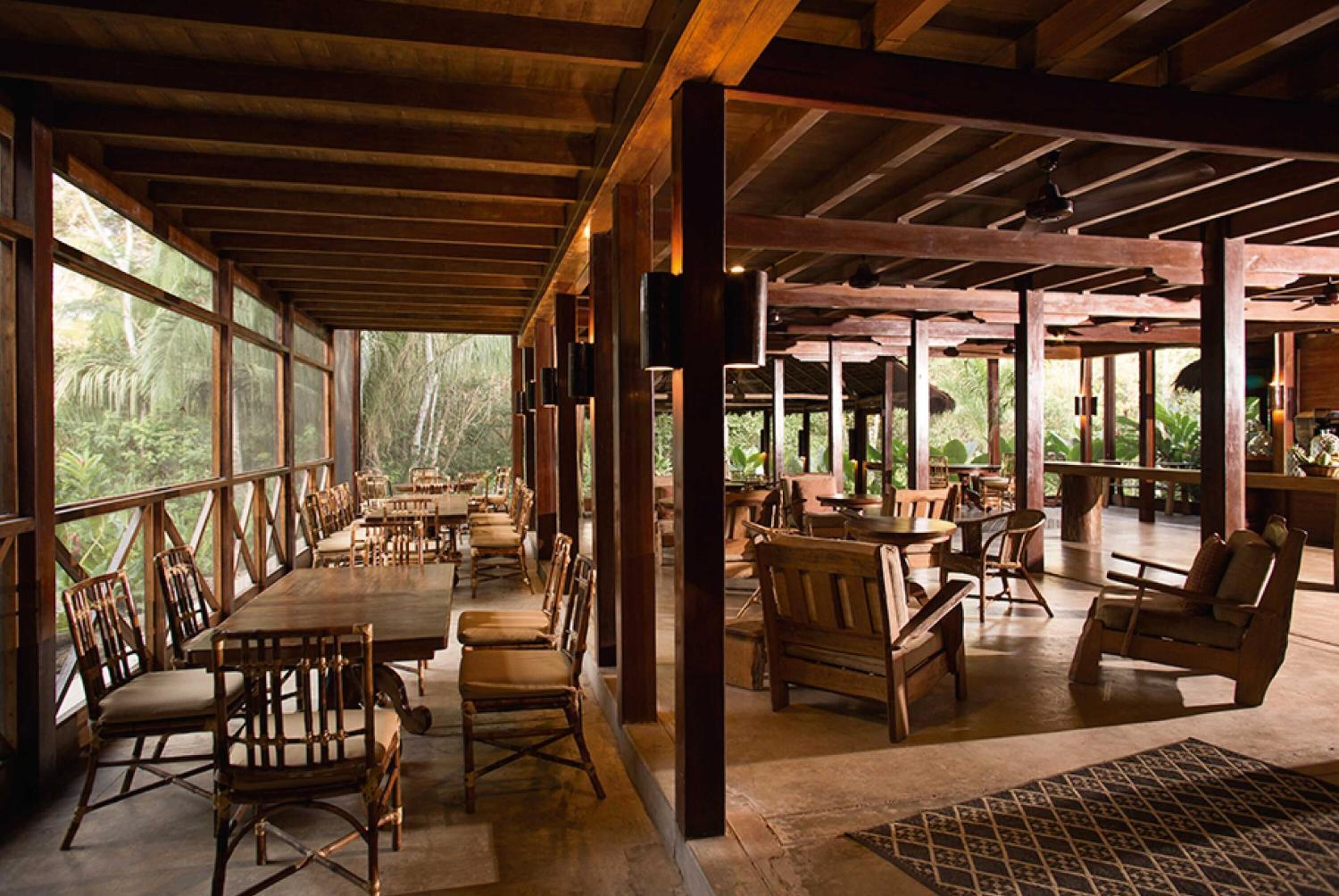 A spacious dining area with wooden tables and chairs, large windows offering views of the surrounding forest.