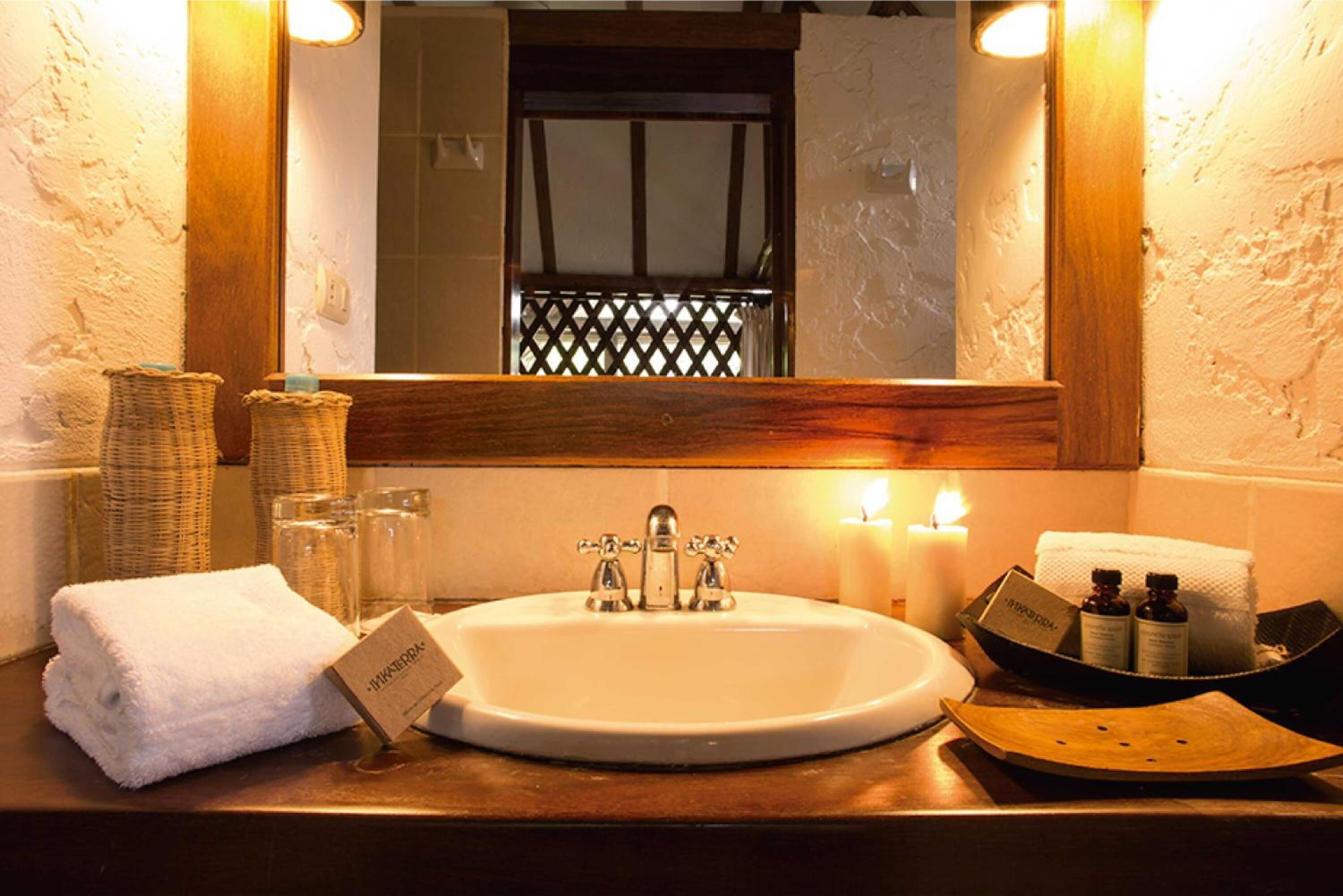 Une salle de bain avec un lavabo blanc, un miroir et des articles de toilette. On y trouve des paniers en osier, une serviette blanche et un plateau avec des flacons.