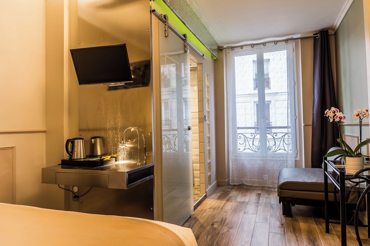 A hotel room with a bed, a desk with a chair, a shower, and a balcony with a view.