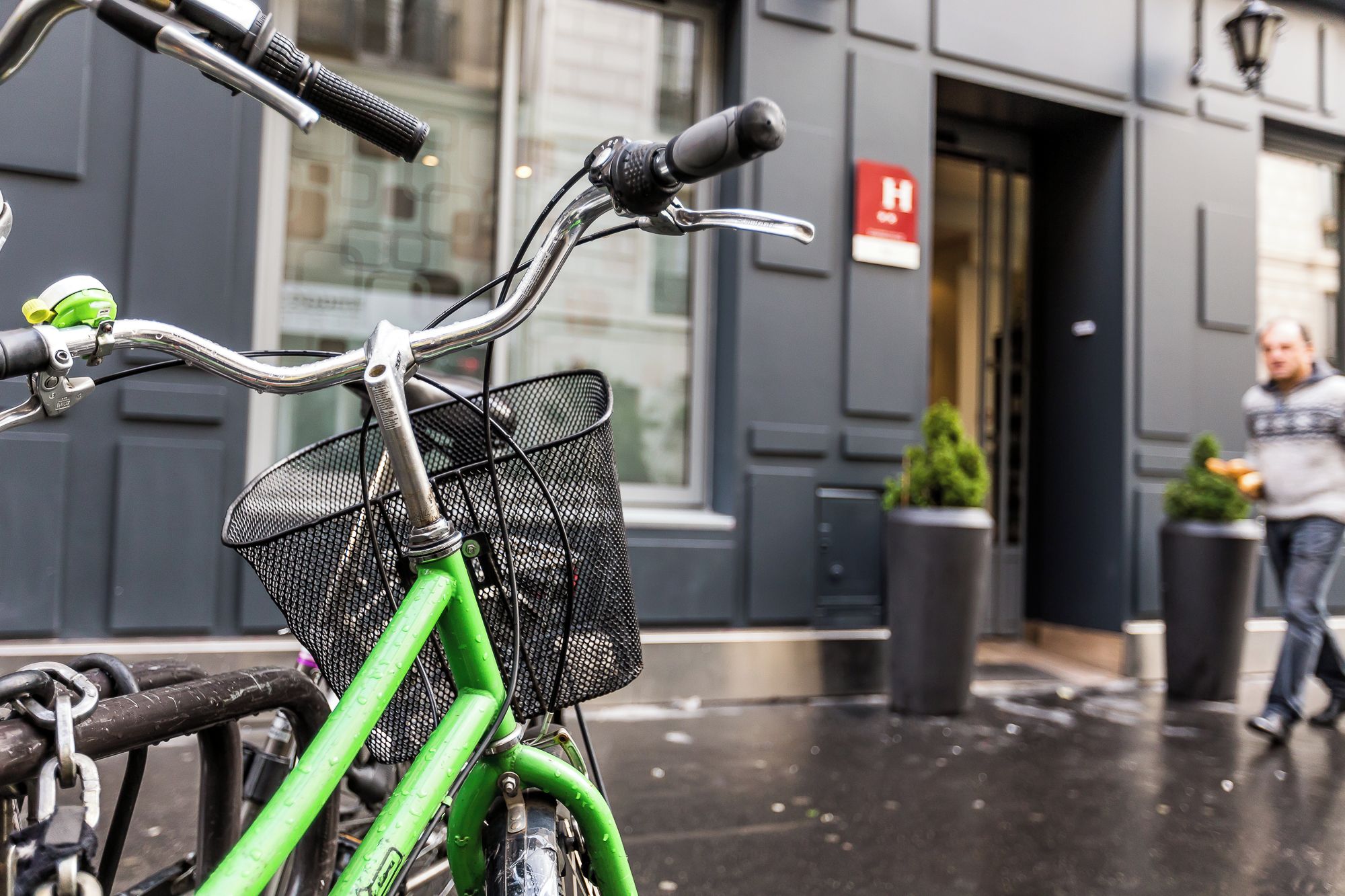 A bicycle with a green frame and a basket, parked in front of a building with a door and a sign.