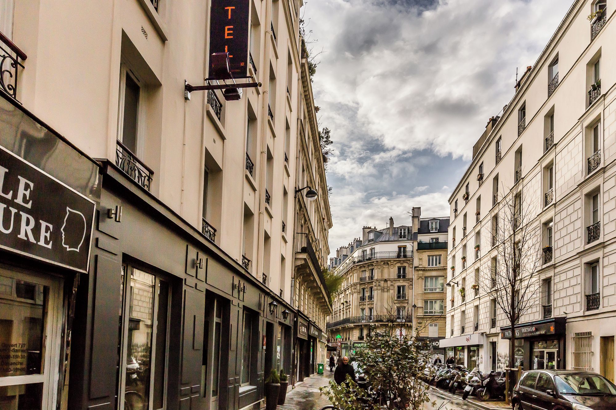 Une rue étroite, bordée de bâtiments des deux côtés, avec une enseigne indiquant un hôtel et des voitures garées.