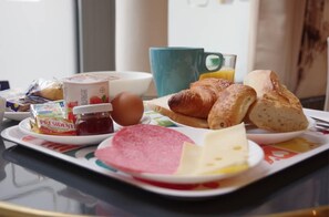 A breakfast tray with croissants, a ham slice, cheese, a boiled egg, a jar of jam, and a cup of orange juice. - District Republique (Paris)