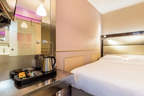 A hotel room with a bed, a bedside table with a kettle and a tray, a mirror, and a shower with a purple light. - District Republique (Paris)