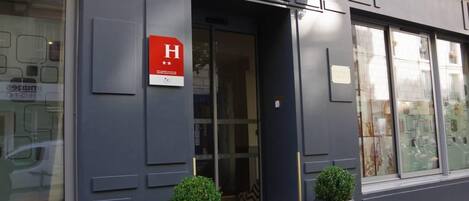 A hotel entrance with a prominent 'H' sign, a glass door, and two potted plants.