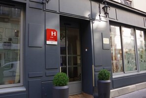A hotel entrance with a prominent 'H' sign, a glass door, and two potted plants. - District Republique (Paris)