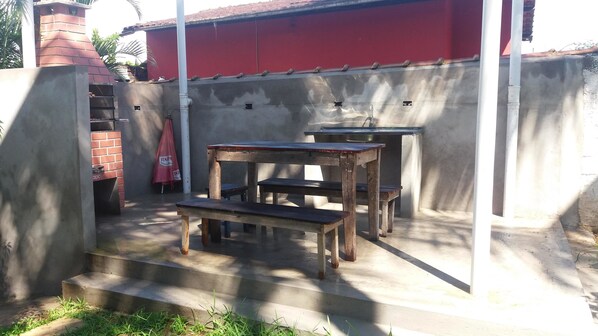 A patio area with outdoor furniture, including a wooden table and benches, and a red wall in the background. - Pousada da Enseada (Guarujá)