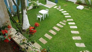 Un petit jardin clos, avec une table et des chaises blanches, un chemin de pierre et des fleurs rouges.