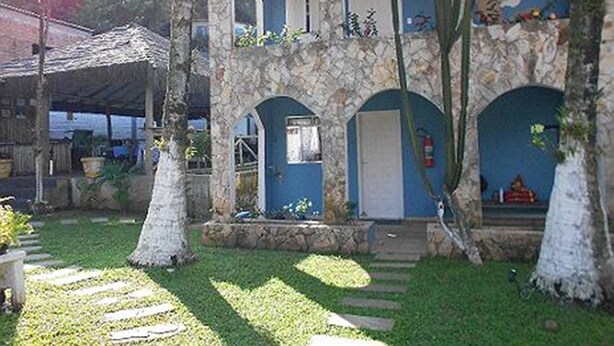 Un bâtiment en pierre aux murs bleus et aux portes cintrées, entouré d’une pelouse bien entretenue et d’arbres.
