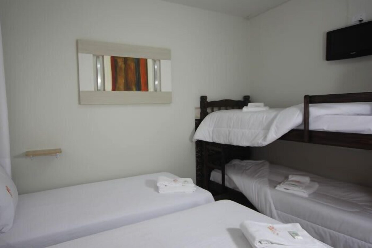 Ein Zimmer mit zwei Einzelbetten, einem Holzkopfstück, einer kleinen Ablage und einem Spiegel an der Wand.