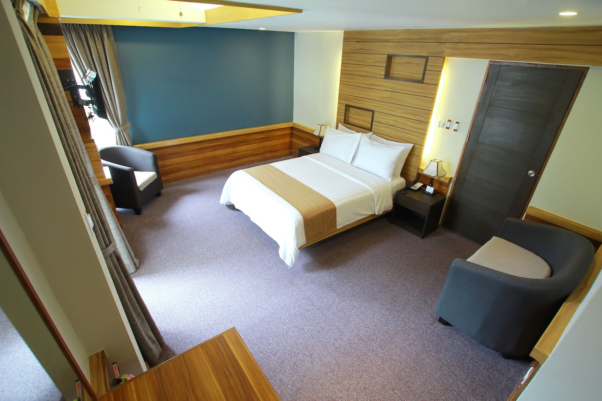 Ein Hotelzimmer mit Bett, Nachttisch, Stuhl und Schreibtisch mit Lampe.