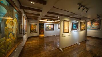 Una galería de arte con pisos y vigas de madera, que exhibe varias pinturas.