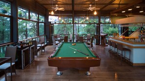 A pool table in a room with large windows, ceiling fans, and a bar area. - Grand Sierra Pines Baguio (Baguio)